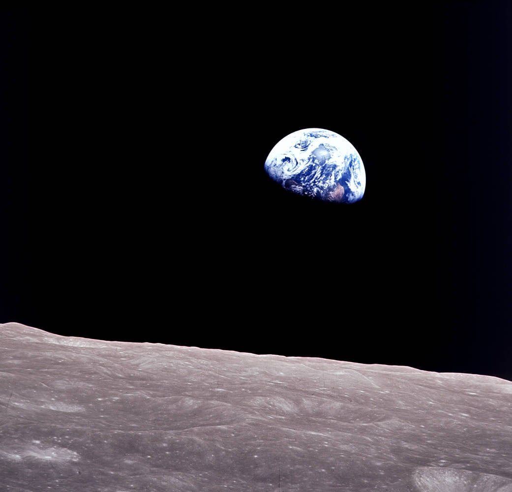 The blue and white Earth rises above the gray lunar horizon against black space